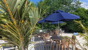 An outdoor patio with tables and chairs, surrounded by a wooden fence and palm trees. - Crosswinds Rehoboth  (Rehoboth Beach)