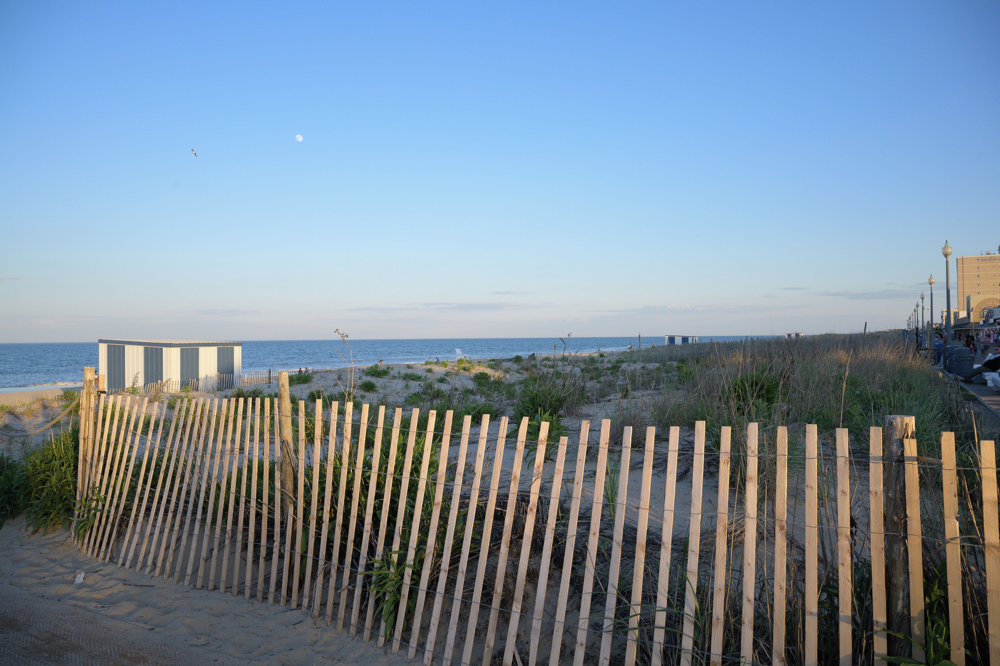 A beach with a wooden fence, a building, and the ocean in the background.