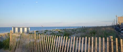 A beach with a wooden fence, a building, and the ocean in the background.
