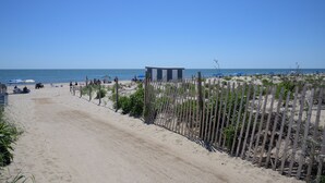 A beach with a sandy path leading to a wooden structure, surrounded by a fence and vegetation. - Crosswinds Rehoboth  (Rehoboth Beach)