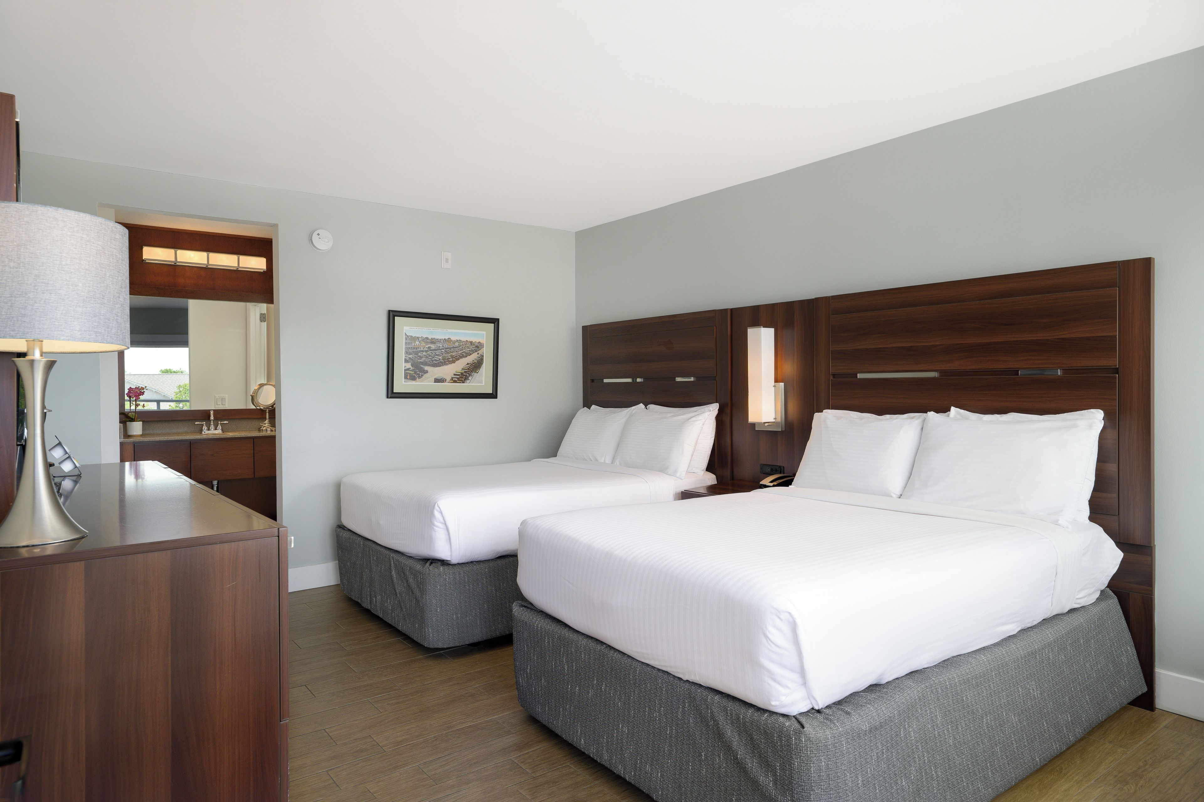 Quarto de hotel com duas camas, uma escrivaninha e um espelho.