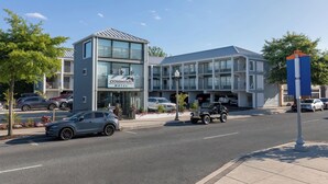 A modern motel with a two-story structure, a covered parking area, and a street view with cars and a motorcycle. - Crosswinds Rehoboth  (Rehoboth Beach)