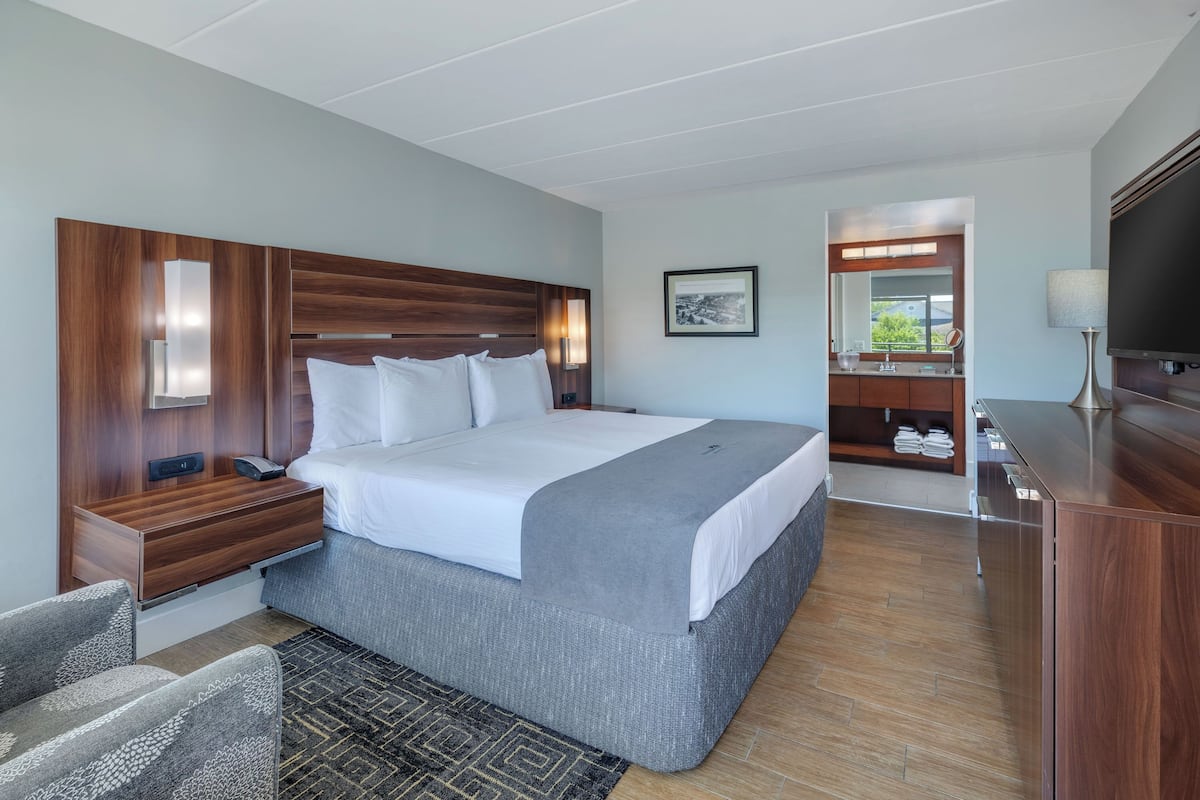 A modern hotel room with a large bed, a desk, a TV, and a bathroom with a mirror and sink.