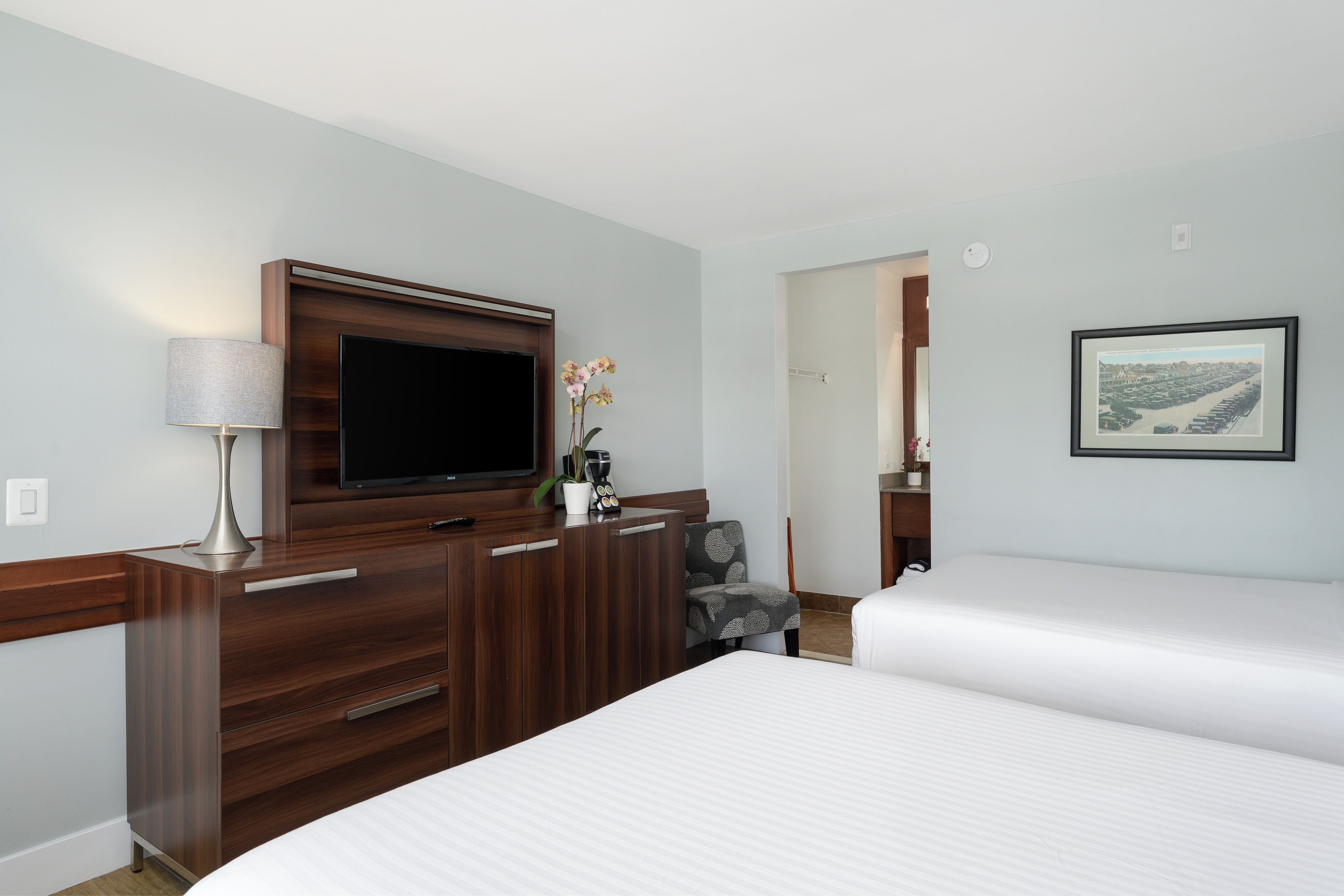 A hotel room with a bed, a TV mounted on a wooden dresser, a lamp, and a framed picture on the wall.