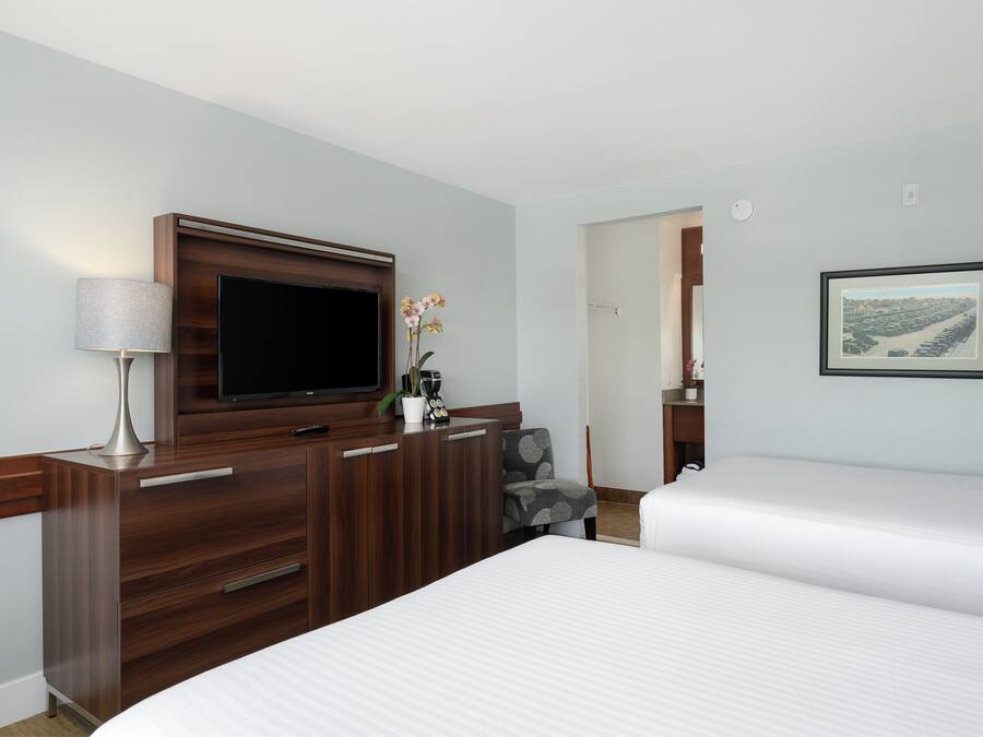 A hotel room with a bed, a TV mounted on a wooden dresser, a lamp, and a framed picture on the wall.