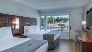 A hotel room with two beds, a TV, a desk, and a large window offering a view of the outside. - Crosswinds Rehoboth  (Rehoboth Beach)