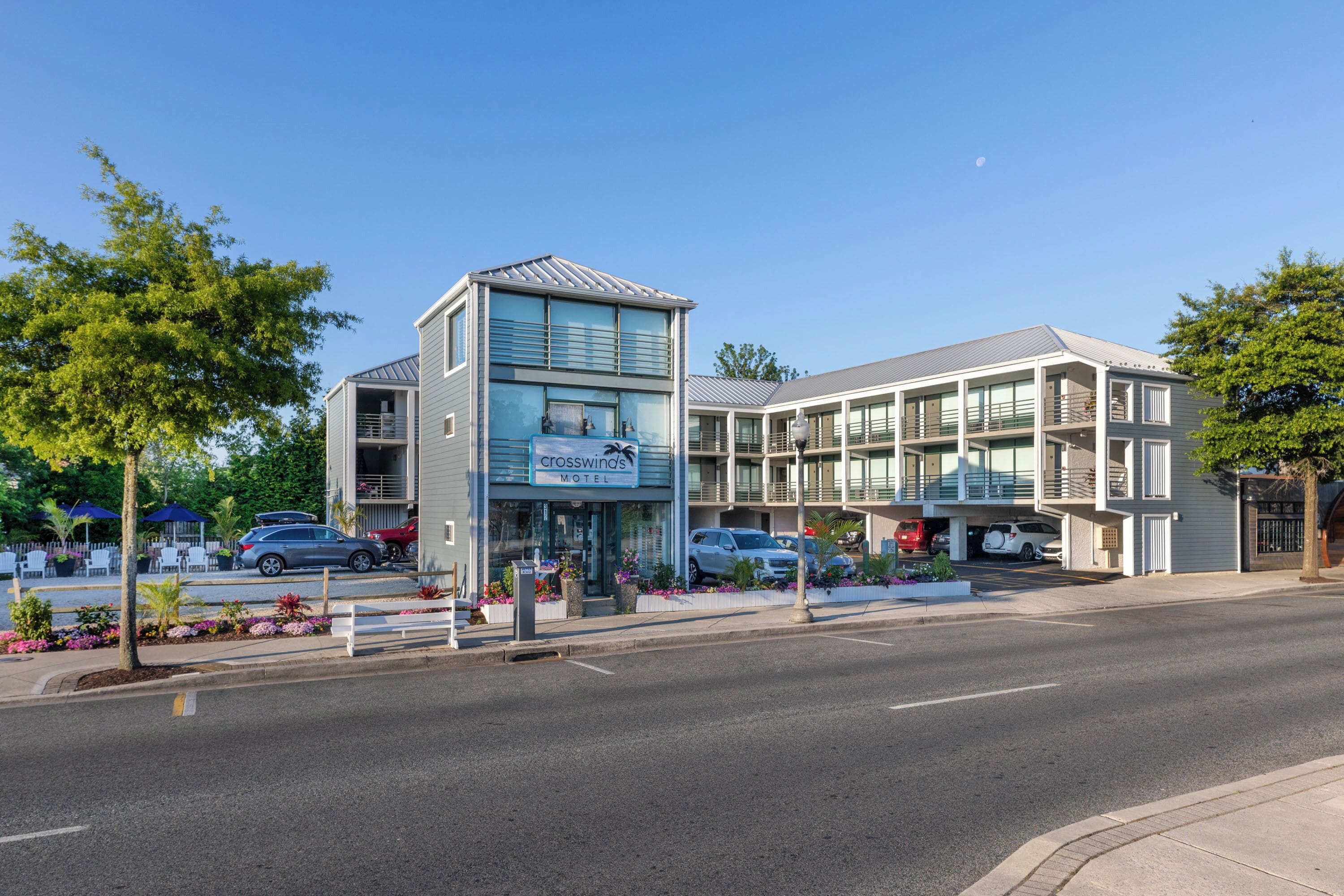Un motel moderno con una estructura de dos pisos, entrada visible y un estacionamiento con varios coches.