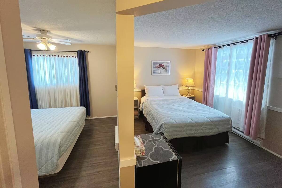 A hotel room with two beds, a ceiling fan, a nightstand with a lamp, and a window with curtains.