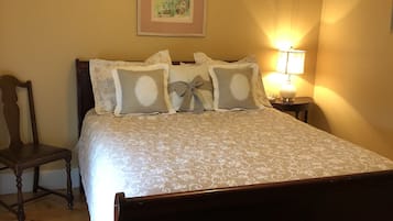Un dormitorio con cama de madera, una mesita de noche con lámpara, un cuadro en la pared y una silla.
