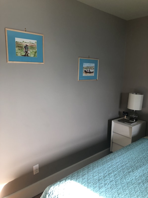 A bedroom with a bed, a nightstand with a lamp, and two framed pictures on the wall.