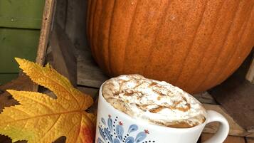 Ein Kürbis, eine Tasse mit Blumenmuster und Herbstlaub auf einer Holzfläche.