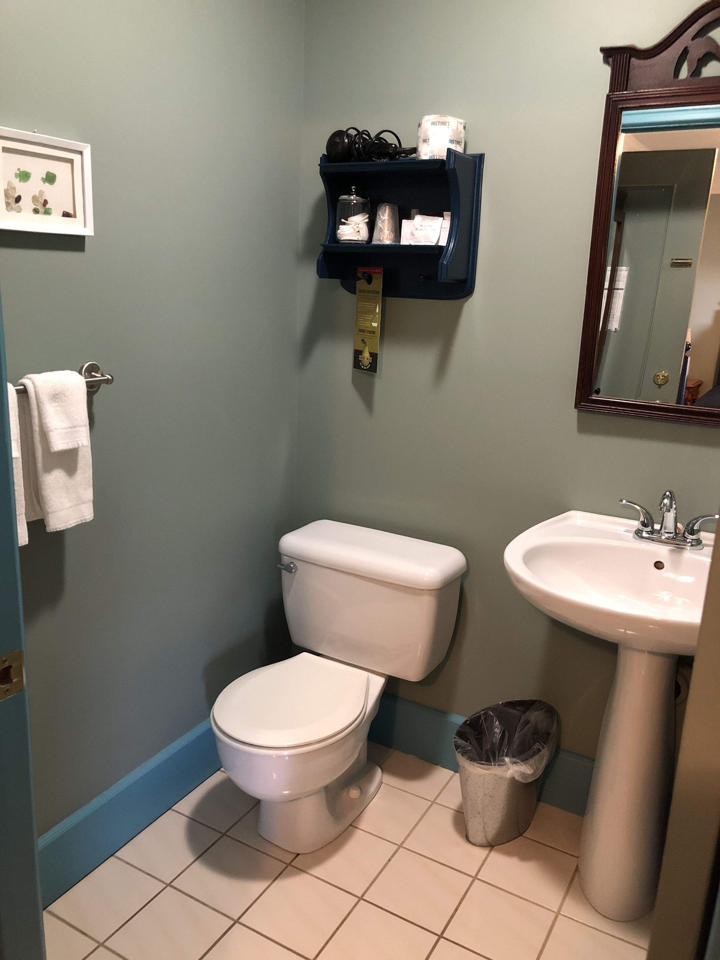 Un baño con inodoro, lavamanos y estante con artículos de aseo.