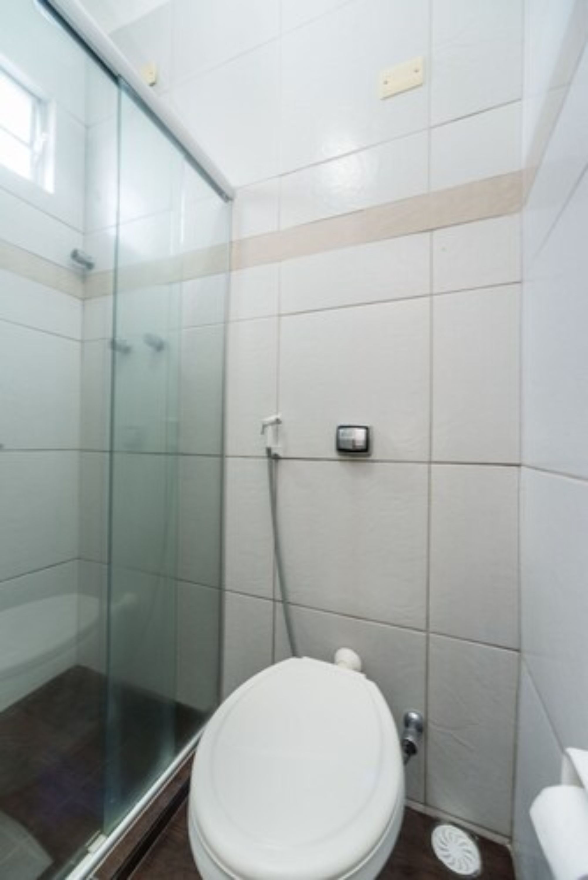 Un baño con cabina de ducha de vidrio, inodoro y grifo empotrado en la pared.