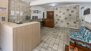 Ein Empfangsbereich mit hölzernem Empfangsschalter, gefliesten Wänden, einer Sitzecke mit einer Couch und einem gefliesten Boden.