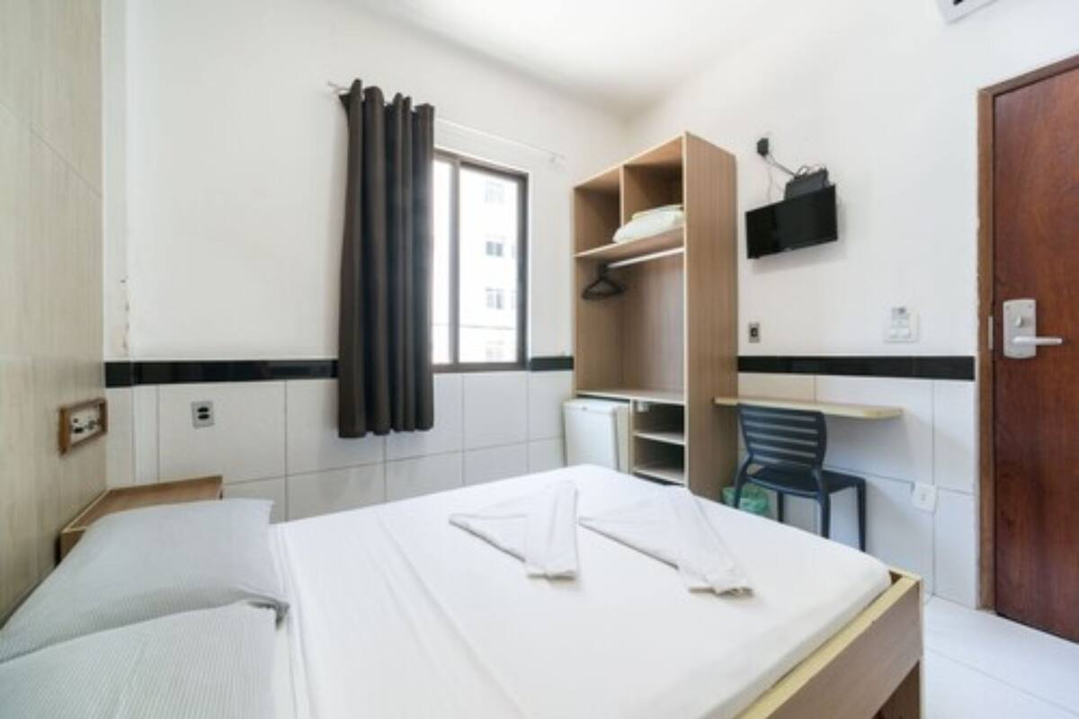 A hotel room with a bed, a desk, a chair, a wardrobe, and a TV on the wall.