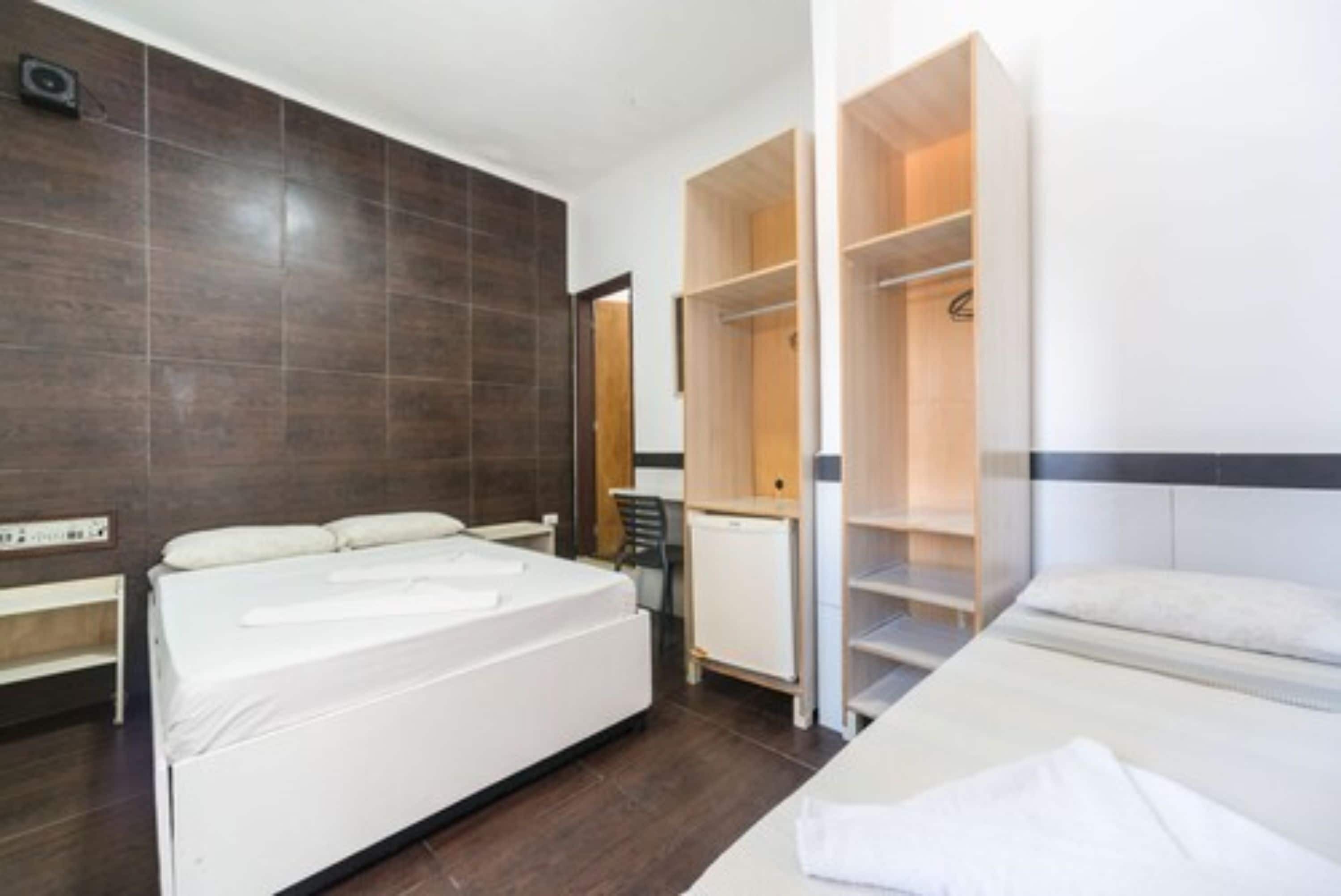 A modern hotel room with a large bed, a wardrobe, and a desk with a chair.