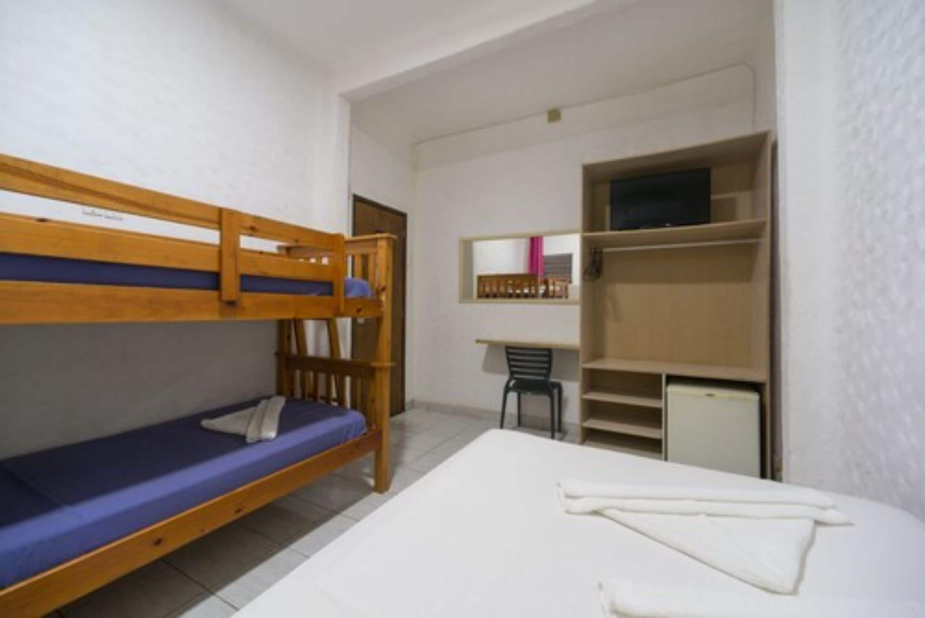 A dormitory room with bunk beds, a desk, a chair, and a small cabinet.