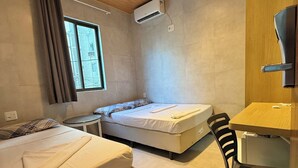 Ein Zimmer mit zwei Betten, einem Schreibtisch, einem Stuhl, einer Klimaanlage und einem Fenster.