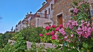 A row of stone houses with balconies, surrounded by lush greenery and pink flowers. - Lions Nine (Zagora-Mouresi)