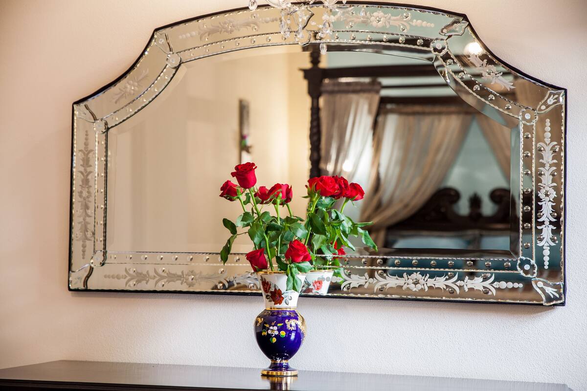A mirror with a decorative frame and a vase with red roses on a table.
