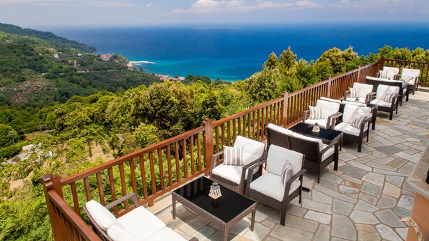 A terrace with wicker furniture and a stone floor, overlooking a coastal landscape. - Lions Nine (Zagora-Mouresi)