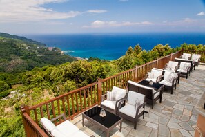 A terrace with wicker furniture and a stone floor, overlooking a coastal landscape. - Lions Nine (Zagora-Mouresi)