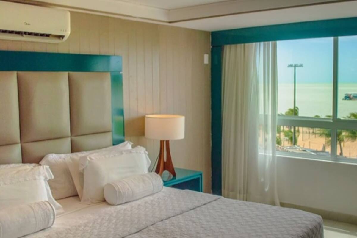 Een hotelkamer met een bed, nachtkastje, lamp en uitzicht op het strand.