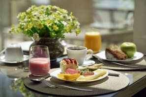 Uma mesa de café da manhã com um prato de comida, um copo de suco, uma xícara de café e um vaso de flores.