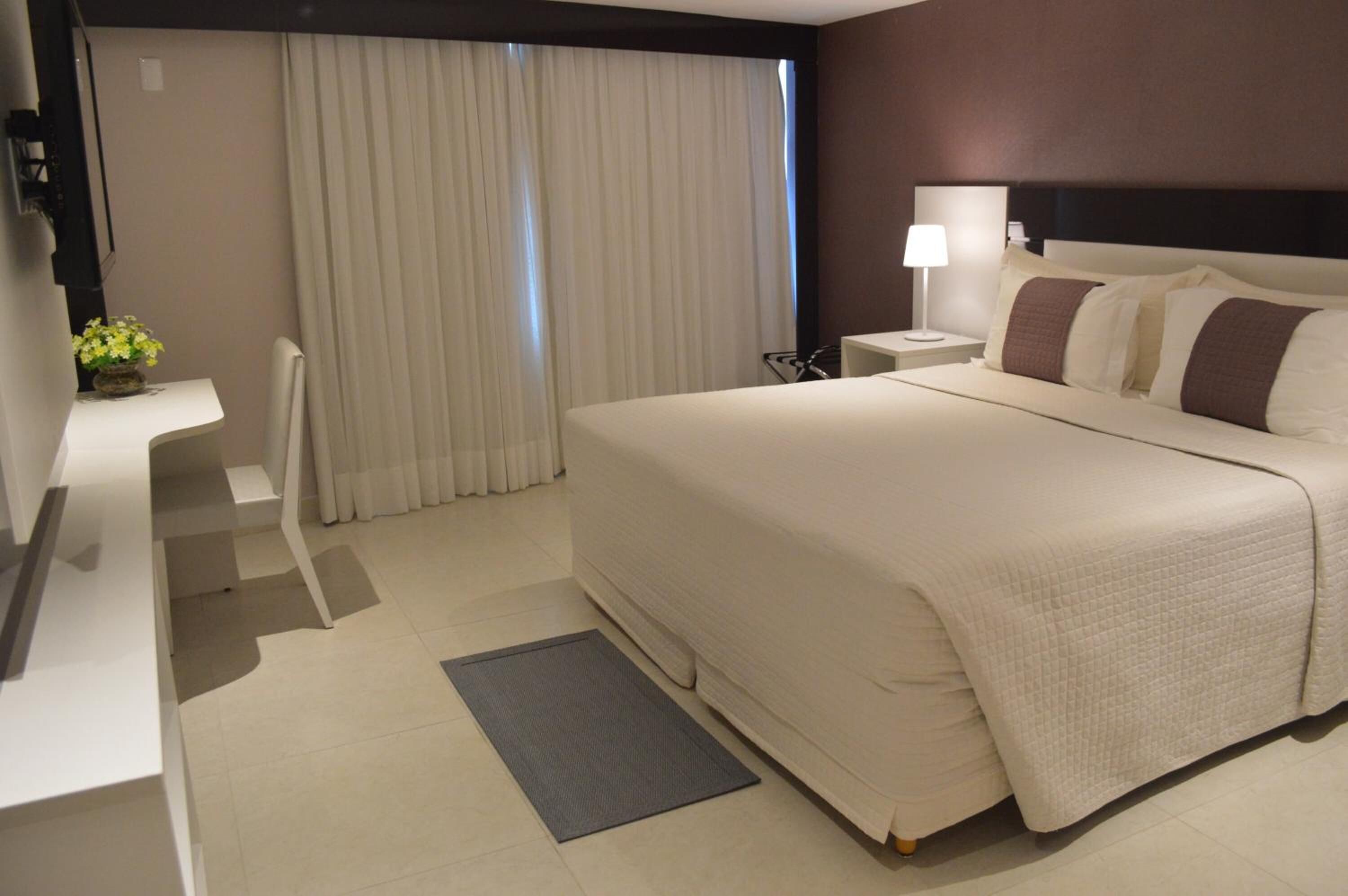 Una habitación de hotel con una cama grande, un escritorio, una silla, una mesita de noche y una lámpara.