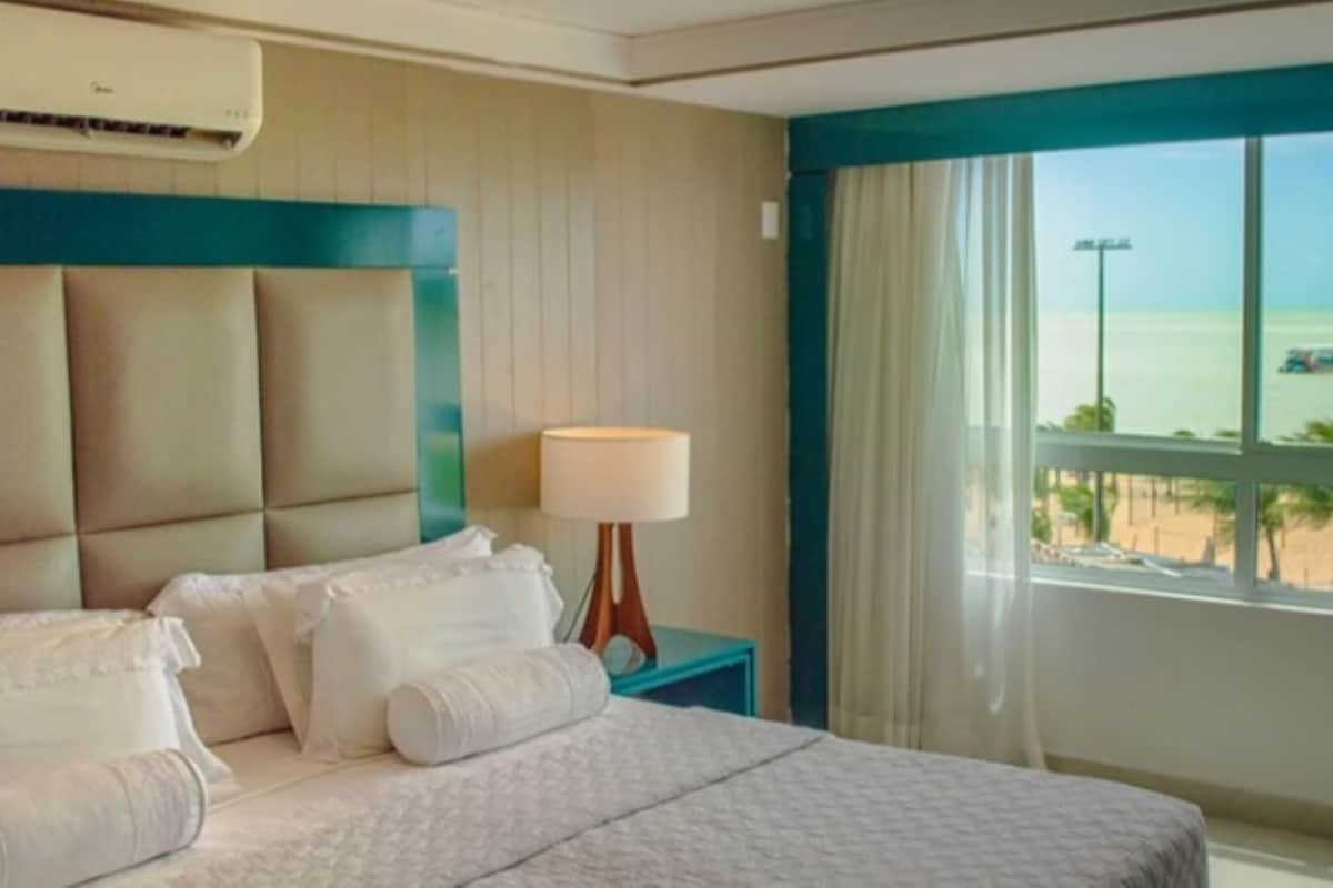 Een hotelkamer met een bed, nachtkastje, lamp en uitzicht op het strand.