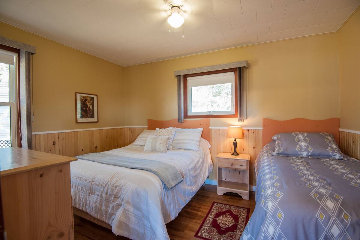 A bedroom with two beds, a window, a nightstand, and a wooden headboard.