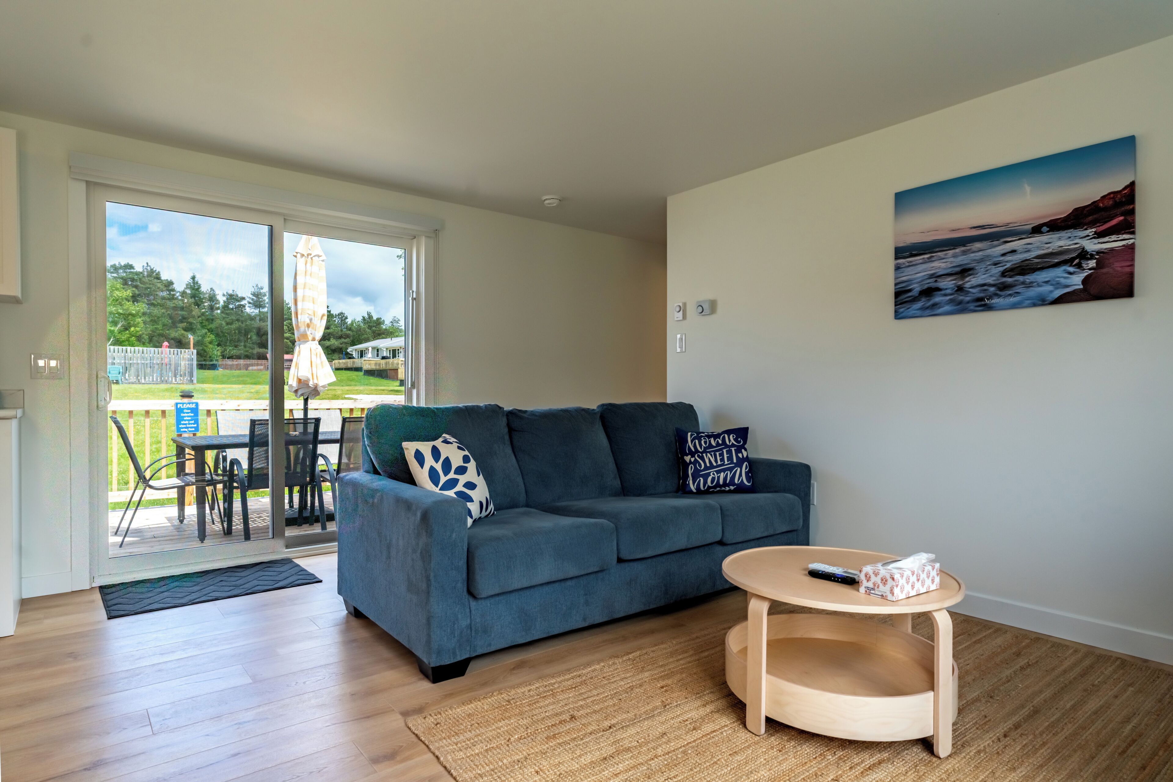 A living room with a blue sofa, a round wooden coffee table, and a painting of a beach scene.