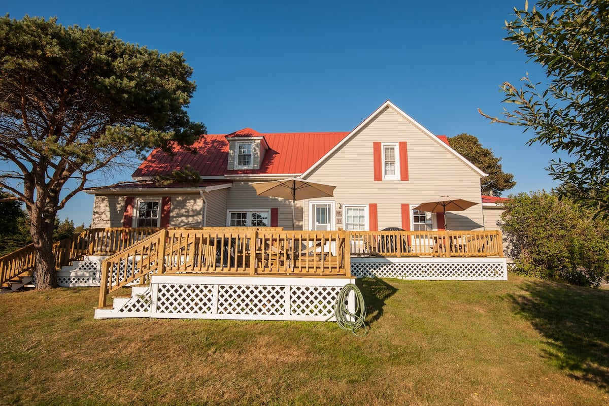 A two-story house with a red roof, white siding, and a wooden deck with a white lattice fence.