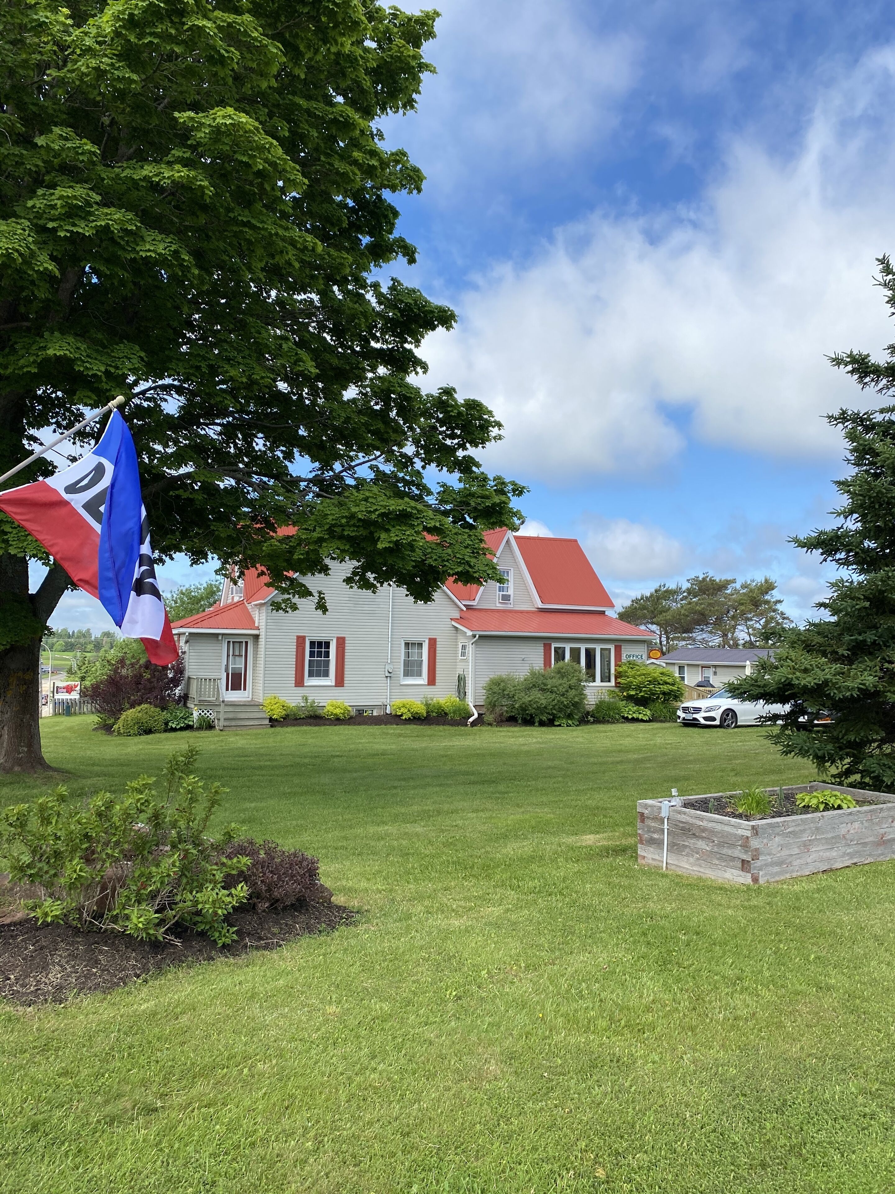 Une maison avec un toit rouge et des murs blancs, entourée d’une pelouse bien entretenue et d’un mât sur lequel flotte un drapeau.