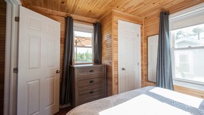 Un dormitorio con paneles de madera, un aparador y un ventanal con cortinas.