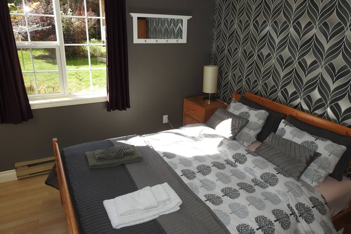 A bedroom with a bed, a nightstand, a window with curtains, and a patterned wall.