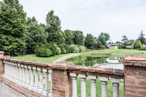 A stone balustrade overlooking a pond with surrounding greenery and a clear sky.