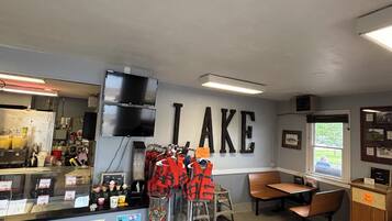 A restaurant interior with a counter displaying food items, a wall with the word "LAKE" above it, and a seating area with tables and chairs.