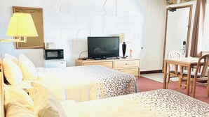 Una habitación de hotel con dos camas, televisión, una mesa con sillas y un espejo.