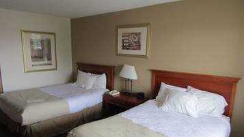 A hotel room with two single beds, a nightstand with a lamp, and two framed pictures on the wall.