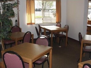 A room with a dining table, chairs, a window with curtains, and a potted plant. - Dakota Inn (Huron)