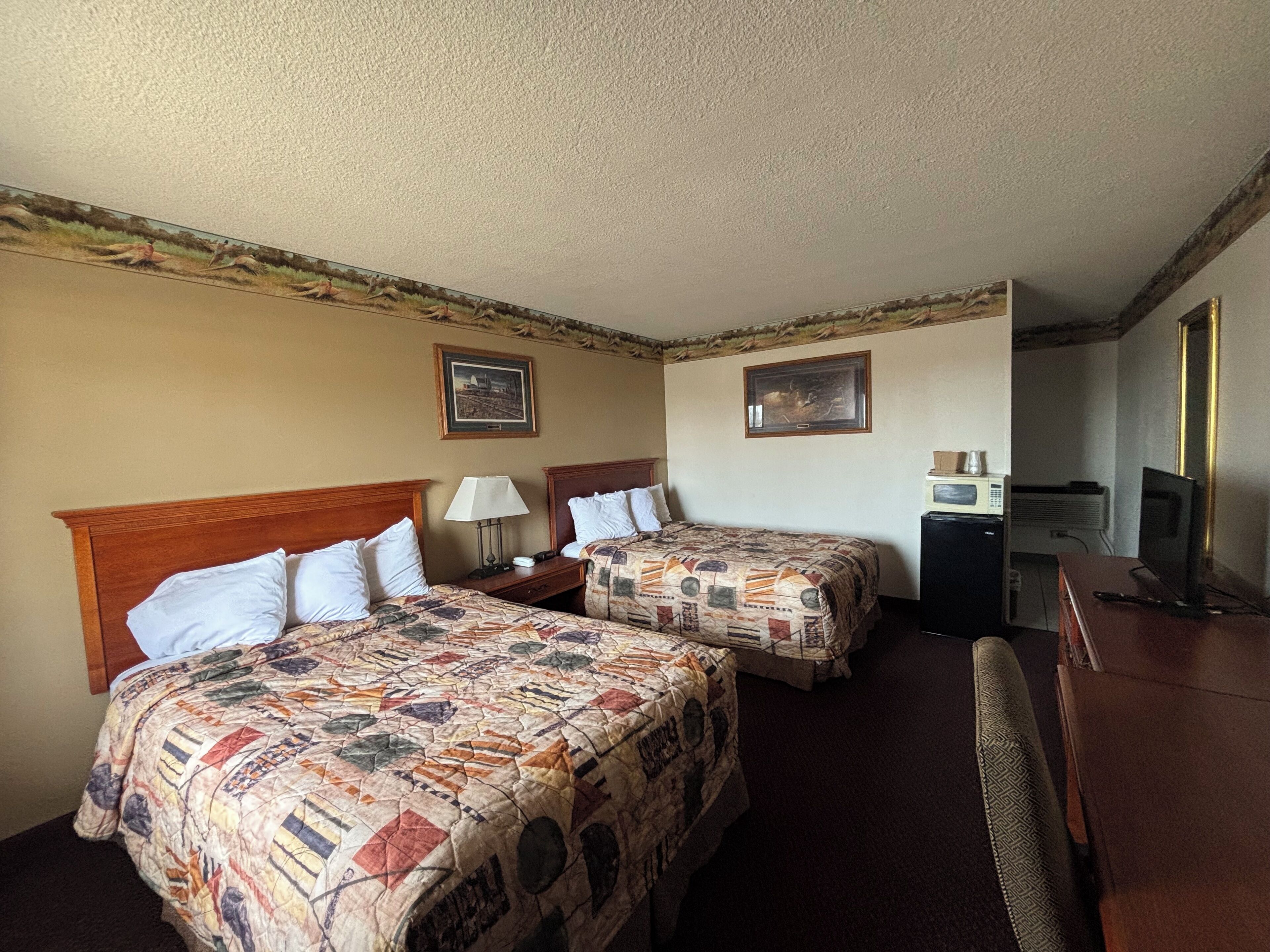 A hotel room with two beds, a desk, a chair, a television, and a microwave.