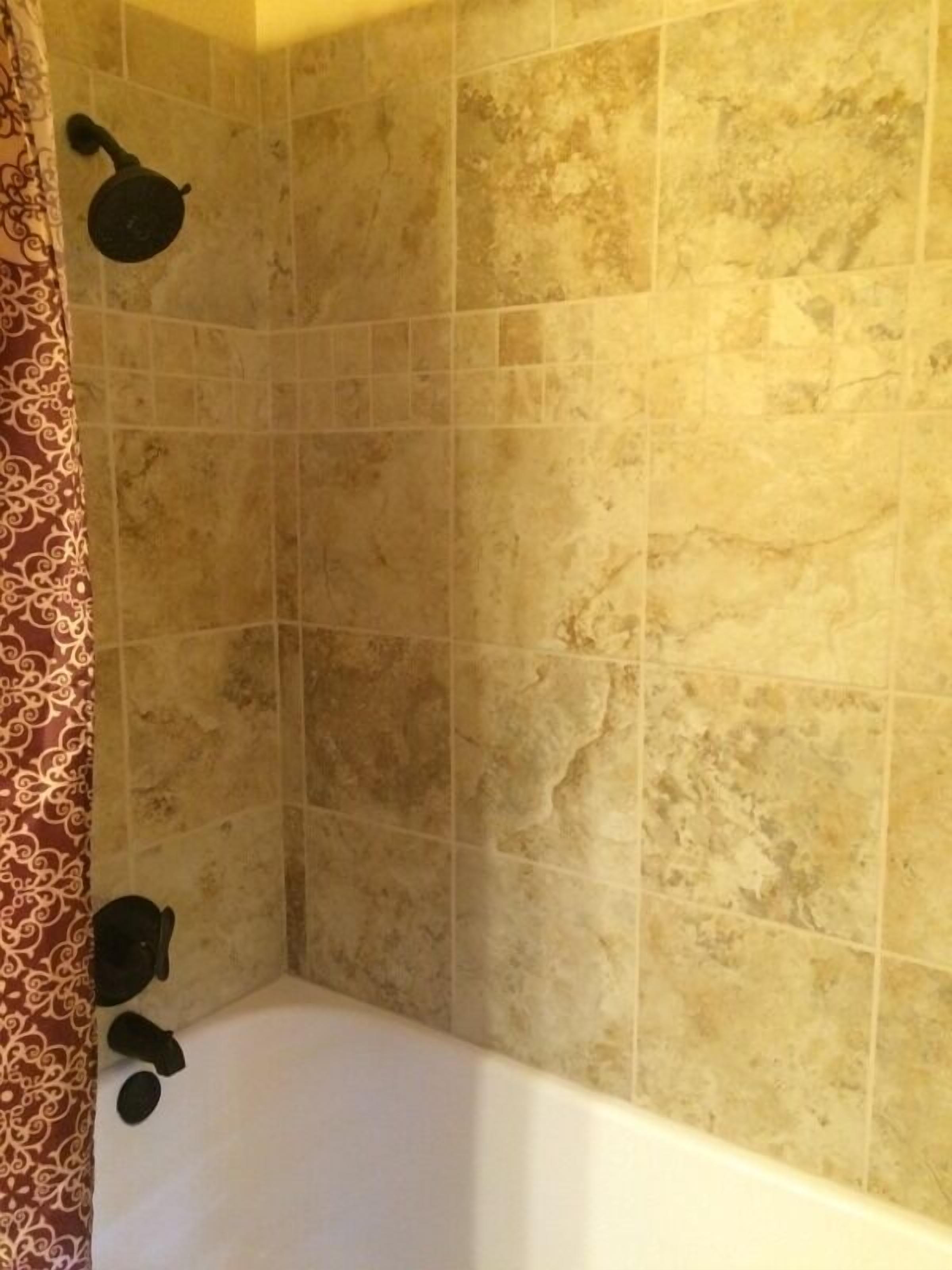 A bathroom with beige tiled walls, a white bathtub, and a shower curtain with a red and white pattern.
