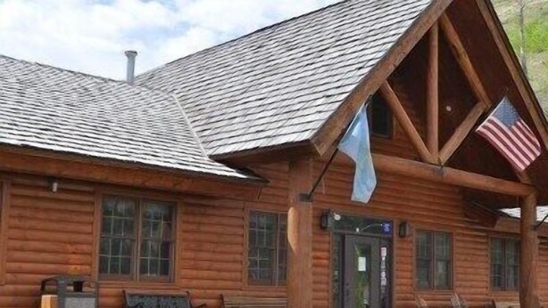 Eine Blockhütte mit Satteldach, einer Veranda mit Bänken und einer amerikanischen Flagge.