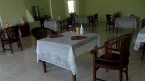 A dining area with tables covered in white tablecloths, wooden chairs, and a tiled floor.