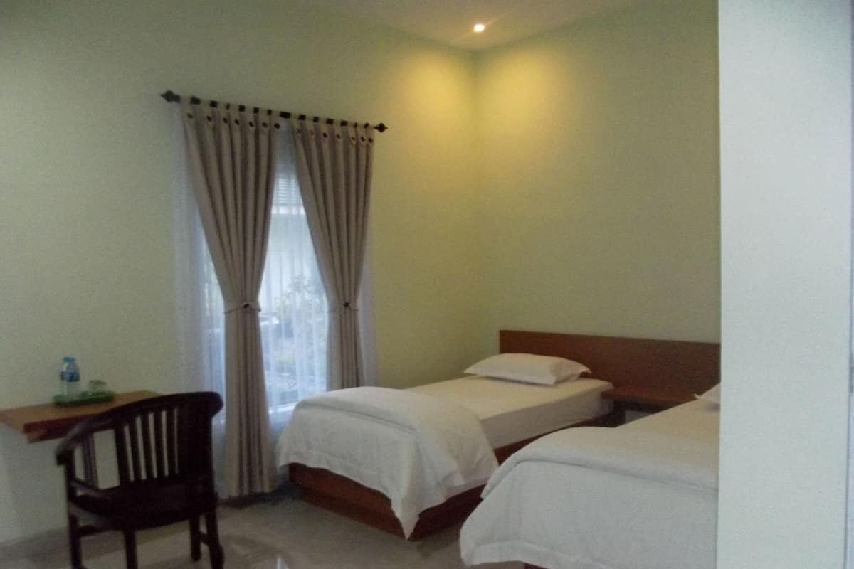 Une chambre d’hôtel avec deux lits, un bureau, une chaise et une fenêtre avec des rideaux.