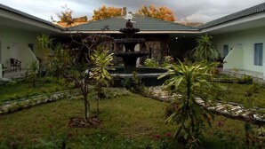 A courtyard with a central fountain, surrounded by tropical plants and a building with a tiled roof.