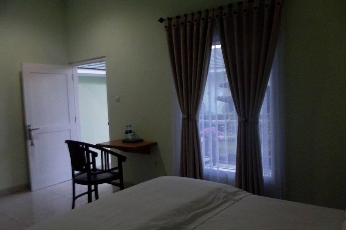 Une chambre à coucher avec un lit, une chaise, un bureau et une fenêtre avec des rideaux.