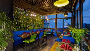 A restaurant with blue seating, wooden tables, and green plants on the walls.