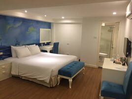 A bedroom with a bed, a desk, a chair, a mirror, and a bathroom with a shower.